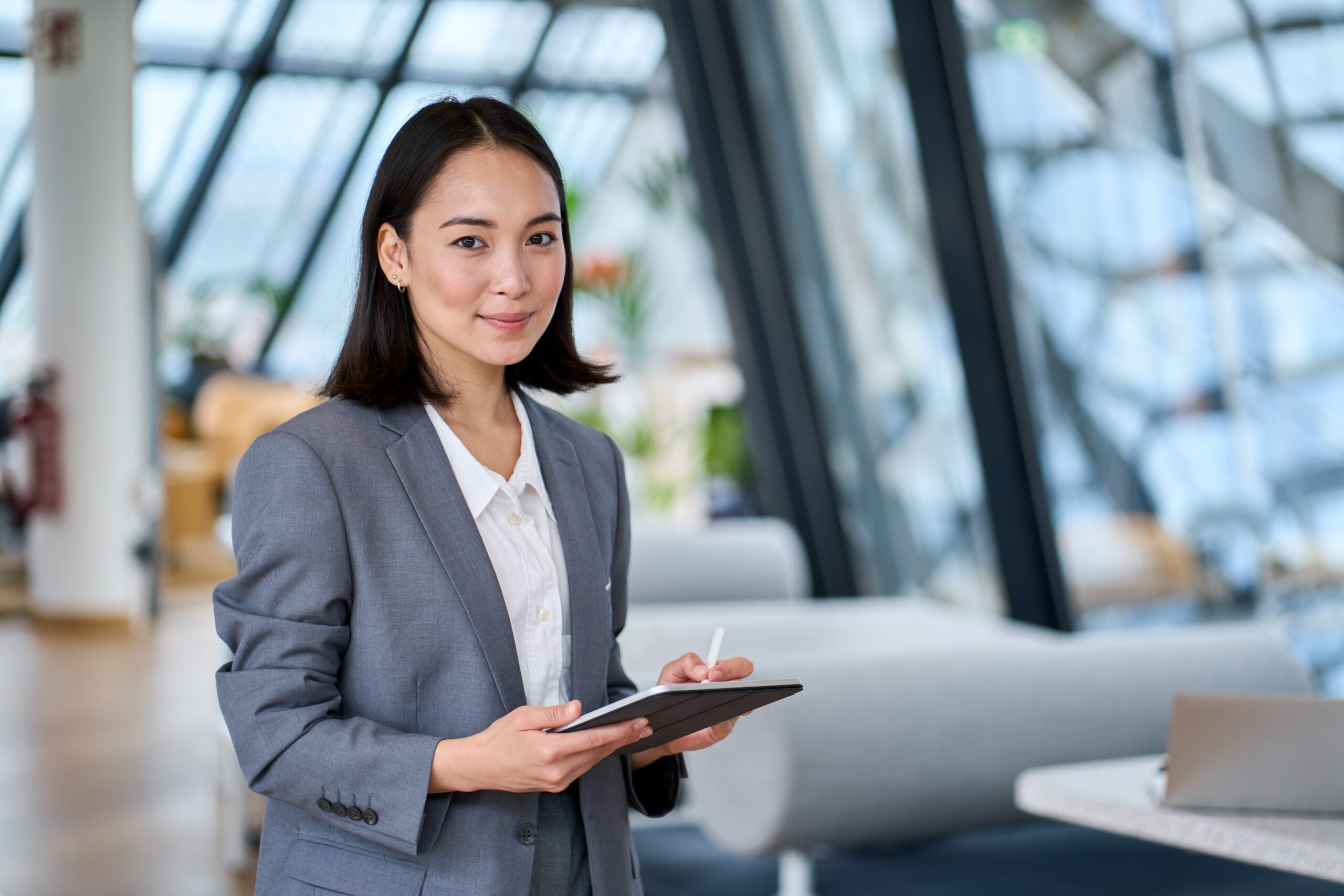 Smiling young Asian business woman leader holding digital tablet in office.